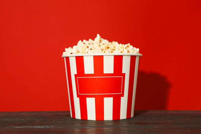 Striped bucket with popcorn against red background, space for text