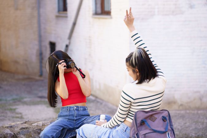 Woman making peace sign above her head and her friend takes her picture