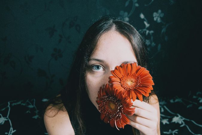 Studio portrait of woman with blue eyes holding gerbera flowers to her left eye