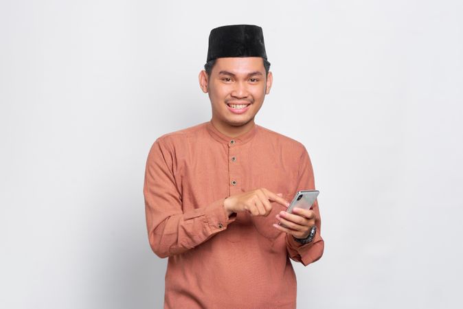 Muslim man in kufi hat smiling and looking up from mobile phone