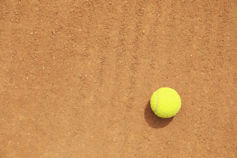 Light green tennis ball on clay court, space for text