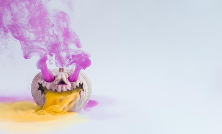 Pumpkin skull with purple and orange smoke on light wall with