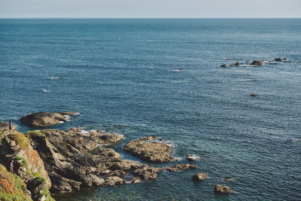 Person standing on a cliff in the distance overlooking the sea