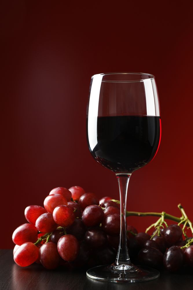 Grapes and glass with wine against red background, copy space