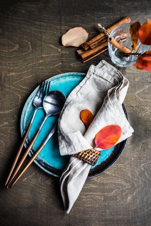 Fall place setting with colorful leaves and cinnamon sticks garnishing teal plate