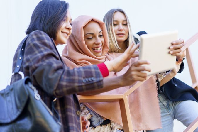 Three happy women selecting something on digital tablet