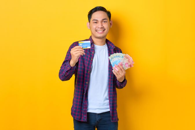 Happy man holding up credit card and cash