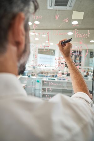 Crop man drawing on glass wall in office