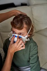 Crop person putting protective mask on kid
