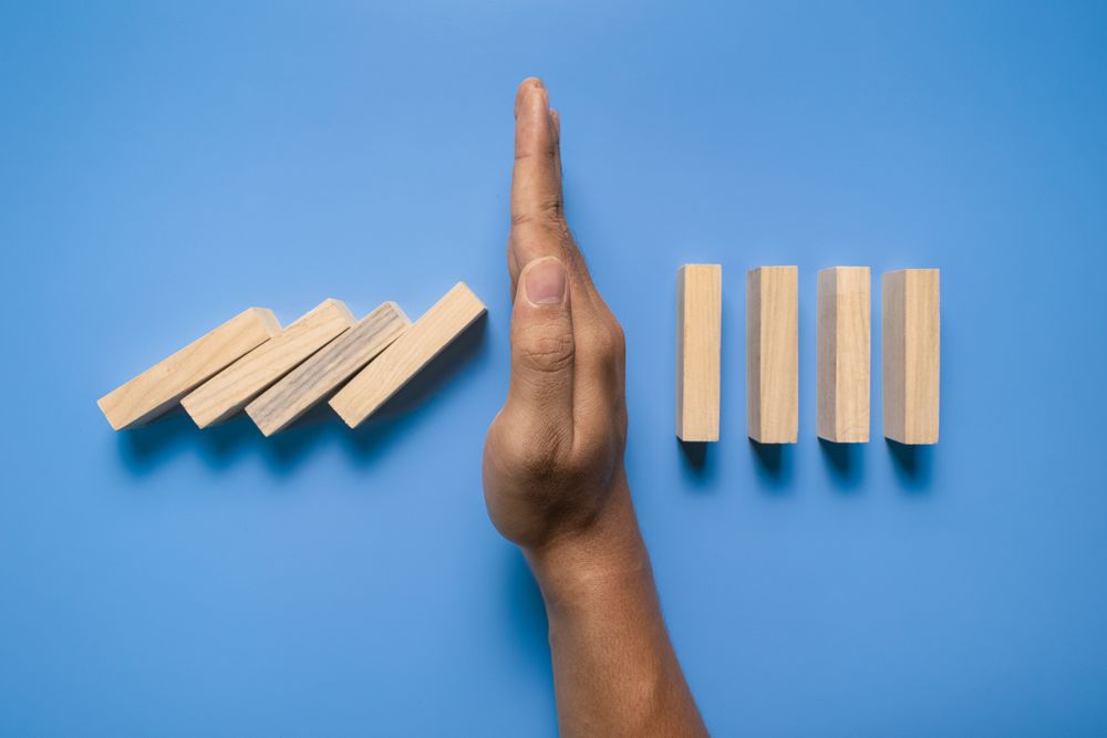 male hand stop falling wooden blocks isolated on blue background. domino effect or risk protection strategy concept