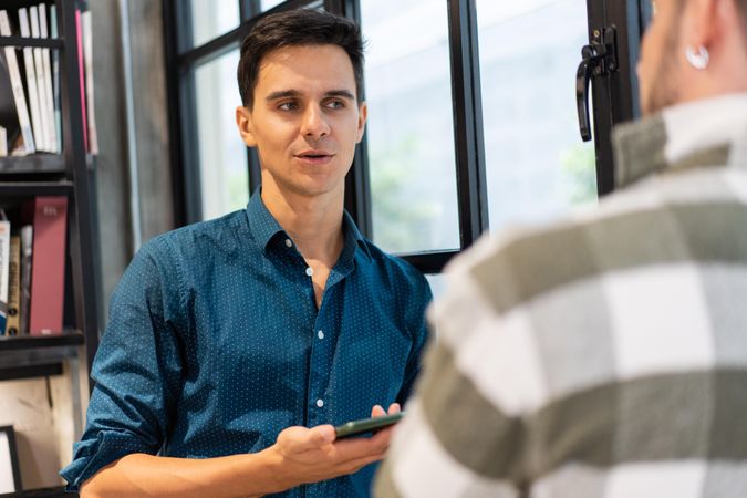 Male employee in shirt holding smartphone chatting with co worker
