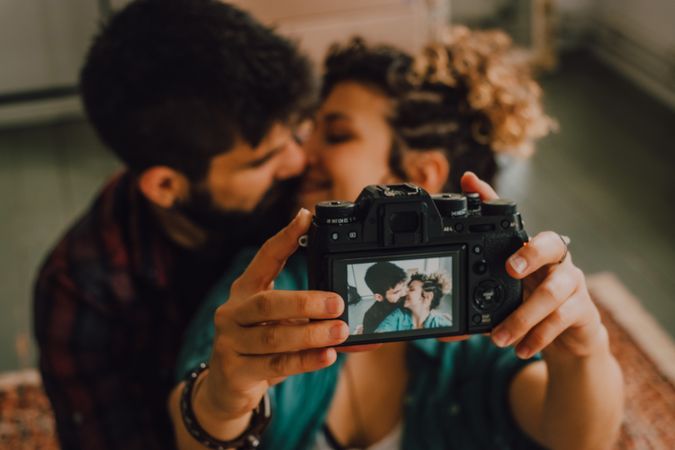 Joyful couple embracing and taking selfie on camera at home
