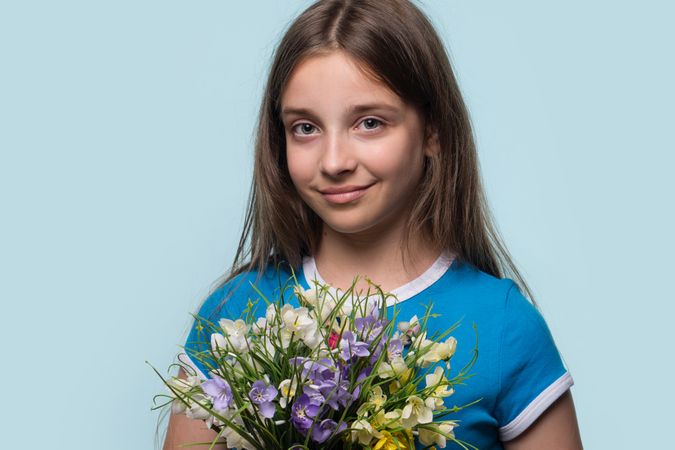 Girl holding bouquet flowers, smiling warmly with gentle expression.