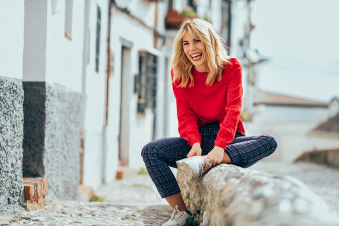 Laughing blonde female with red shirt sitting outdoors