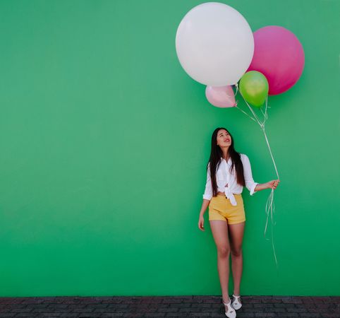 Smiling woman holding a bunch of balloons against a green wall