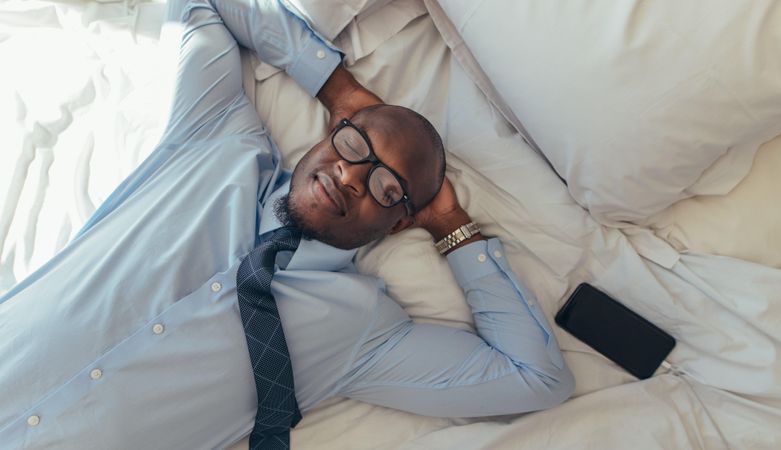 Man in formal clothes relaxing on bed with his eyes closed
