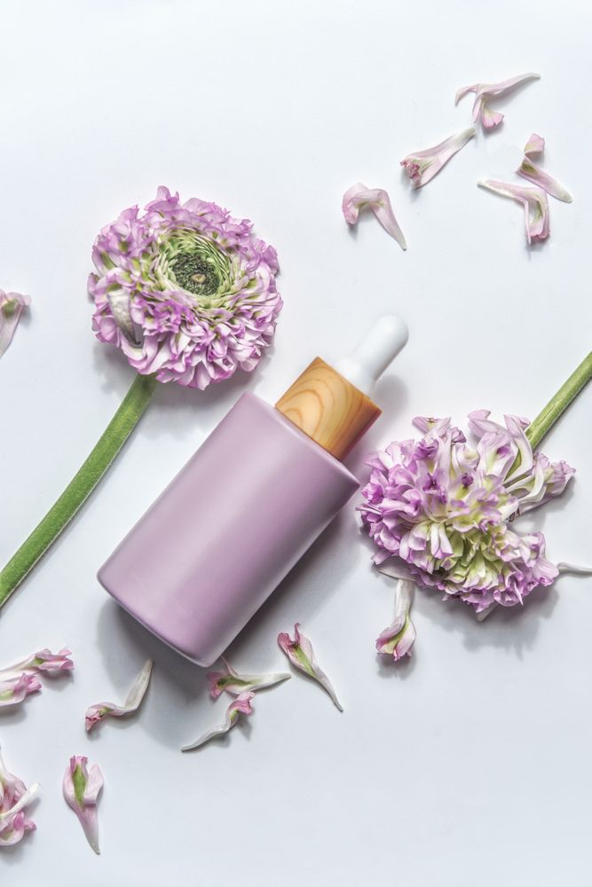 Pastel purple cosmetic bottle with pipette and beautiful flowers and petals