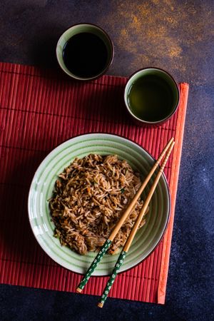 Green bowl of rice with chopsticks on red table setting