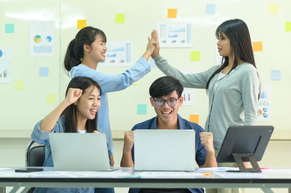 Team of young people cheering with laptop and tablet.