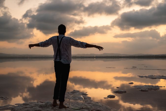 Relaxed man standing with outstretched hands with empty fish tank at shore
