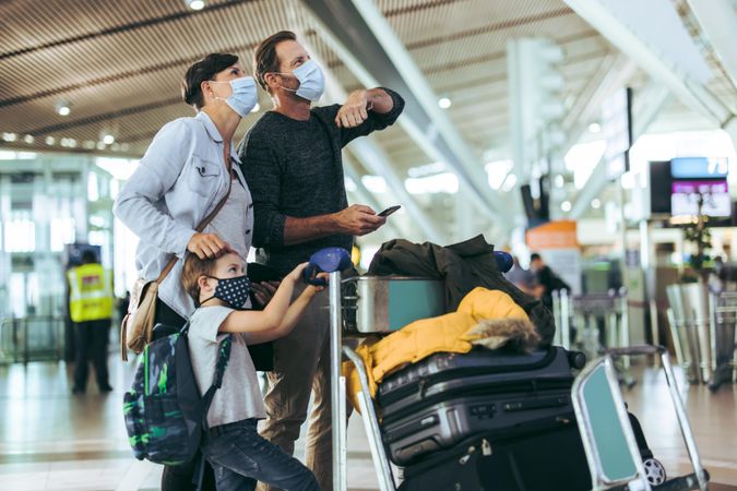Family in face masks looking at their flight times on board at airport