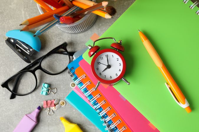 Pile of colorful notebooks with alarm clock, pencils and stationary