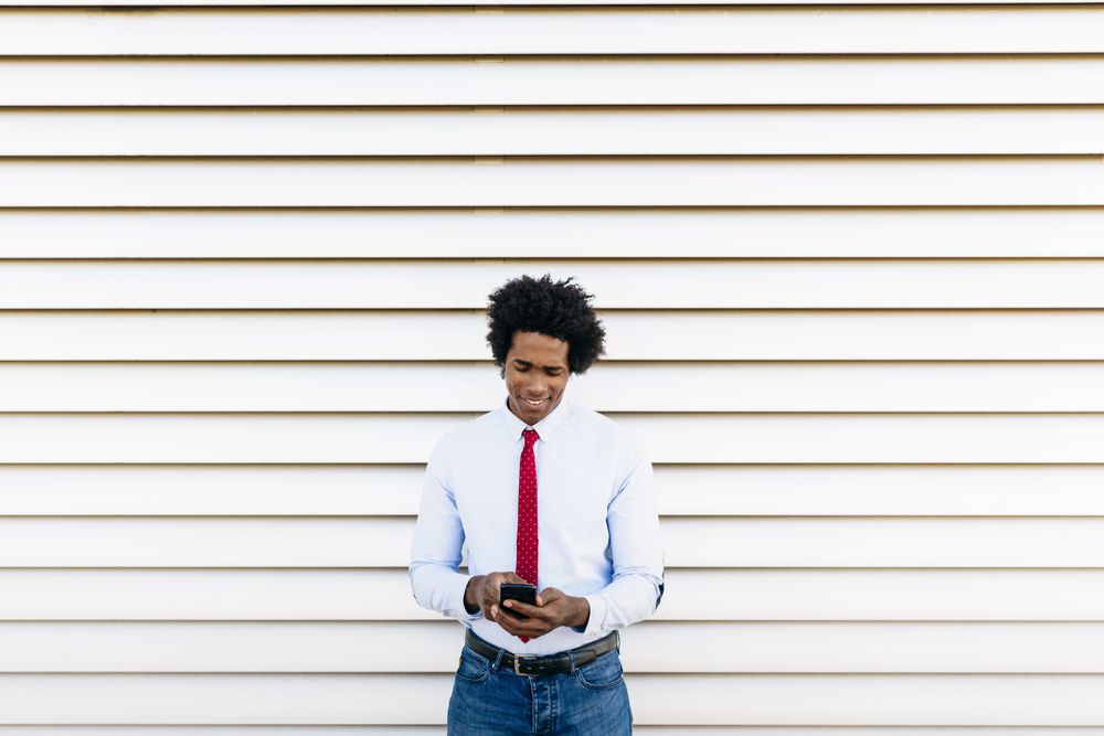 Man in jeans and dress shirt and tie looking down at his phone