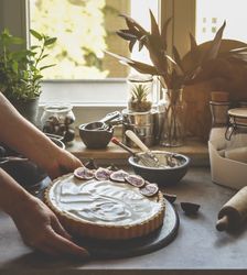 Woman hand holding homemade cheesecake with figs at kitchen background with window and natural light