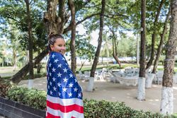Content woman smiling wrapped in American flag walking along park