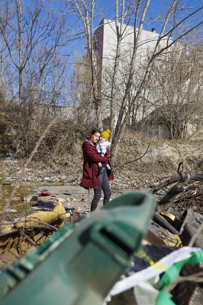 Sad woman holding her baby in garbage filled clearing