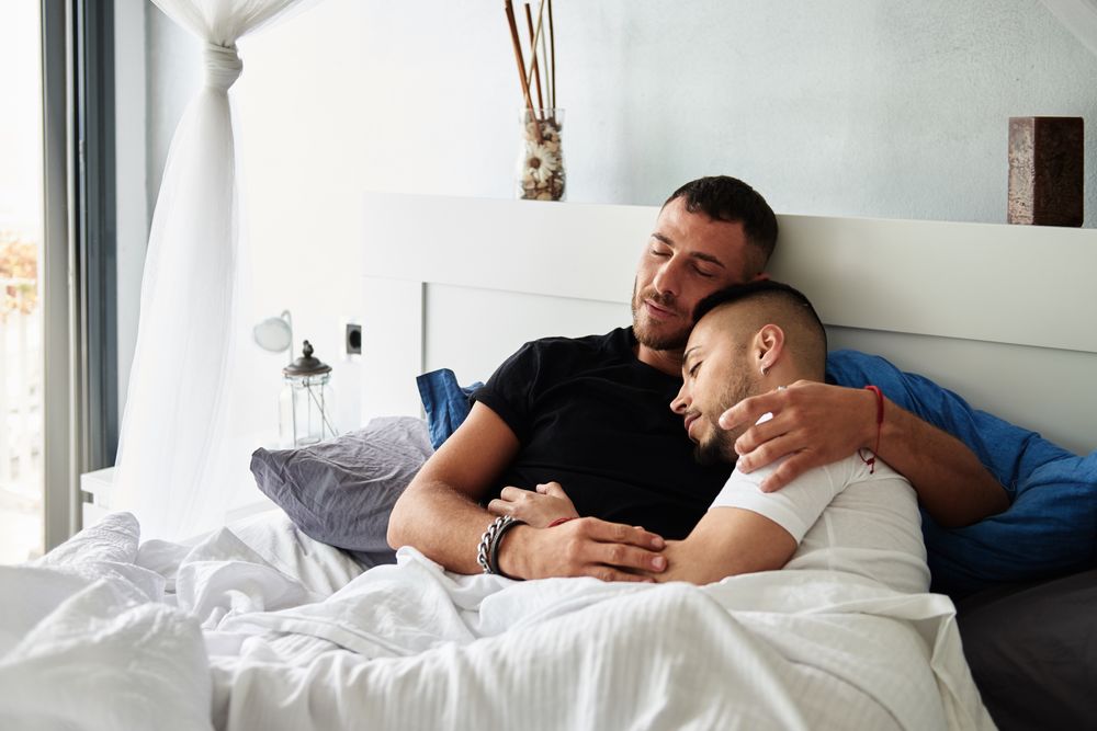 Smiling gay couple hugging on bed