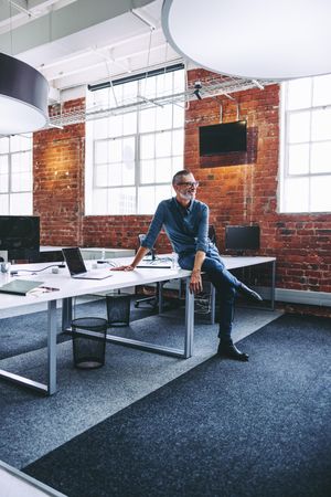 Happy mature businessman sitting alone on an office desk in modern office