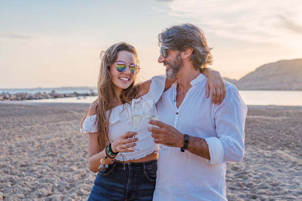Father hugging daughter and clinking glasses on beach