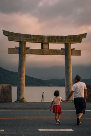 Back view of father and daughter holding hands near a Shinto shrine at sunset in Itoshima, Fukuoka, Japan