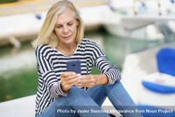Older woman using her smartphone sitting on the dock bDx7yb