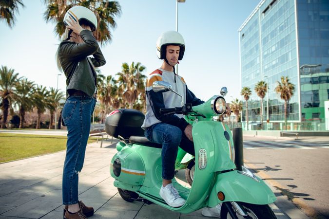 Woman standing regulating helmet and man sitting on bike