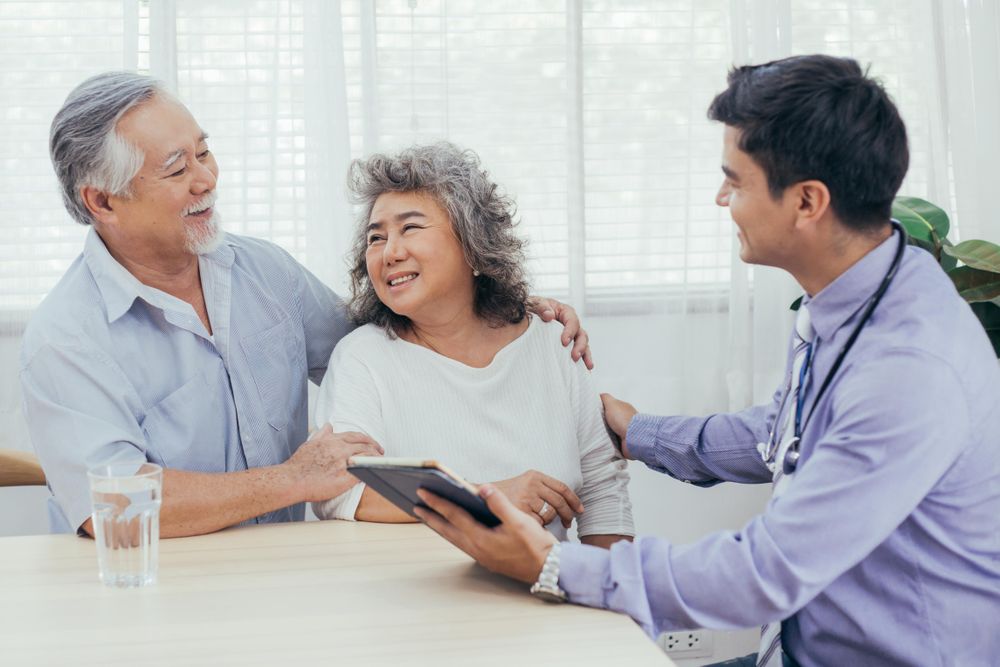 Asian doctor using tablet discussing test result and diagnosis with happy couple