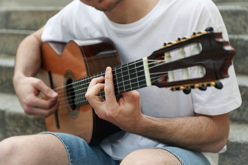 Young man sits on the steps and play on guitar