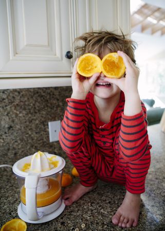 Boy's wearing red striped pajama holding a squeezed orange in kitchen
