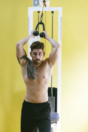 Shirtless male in gym working out his arms using weights machine