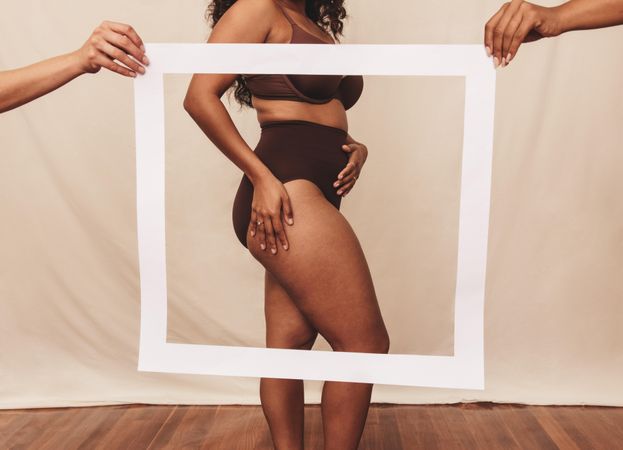 Anonymous biracial woman standing behind a picture frame in brown undergarments