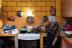 A woman is preparing red chili sauce to go with battered poblano chiles using a gas stove