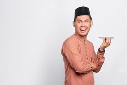 Muslim man in kufi hat talking on speaker phone with copy space