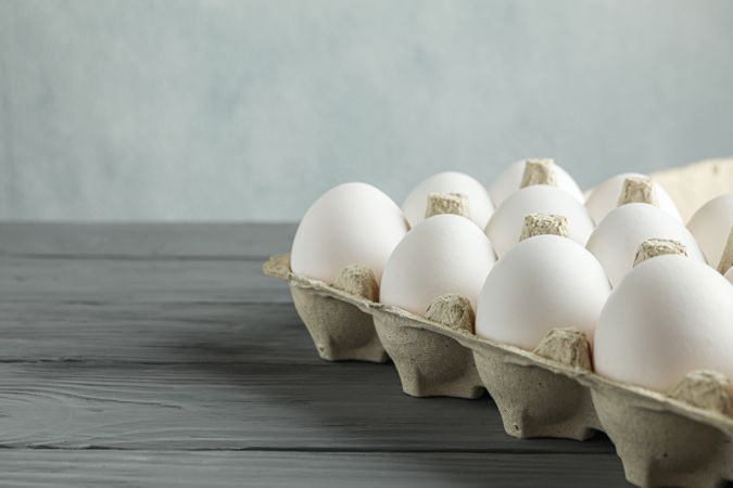chicken eggs in carton box on wooden table against light background, space for text