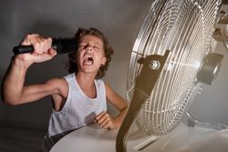 Excited preteen boy shouting into comb in front of working fan