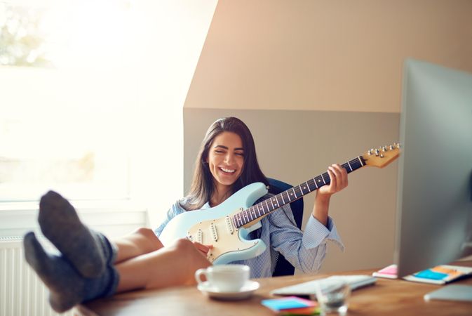 Woman smiling and playing guitar at her desk