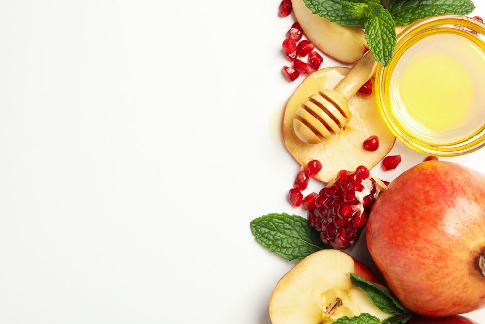 Top view of glass honey pot with dipper, pomegranate, and an apple in corner with copy space
