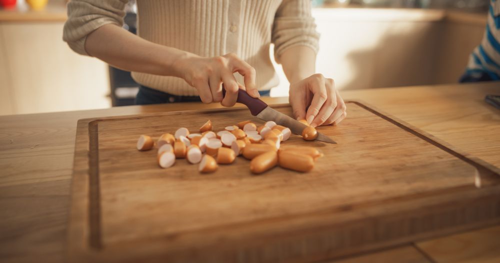 Close Up on the Hands of a Woman Cutting Sausages in her Kitchen at Home.