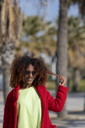 Happy female with hand to her curly hair on street with palm trees