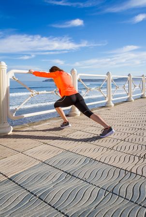 Fit woman stretching legs before running on the beach promenade on a summer morning